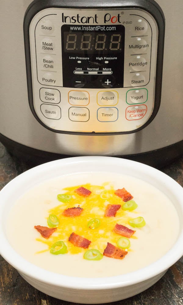 A bowl of potato soup topped with cheese, bacon, and green onions sitting in front of an Instant Pot.