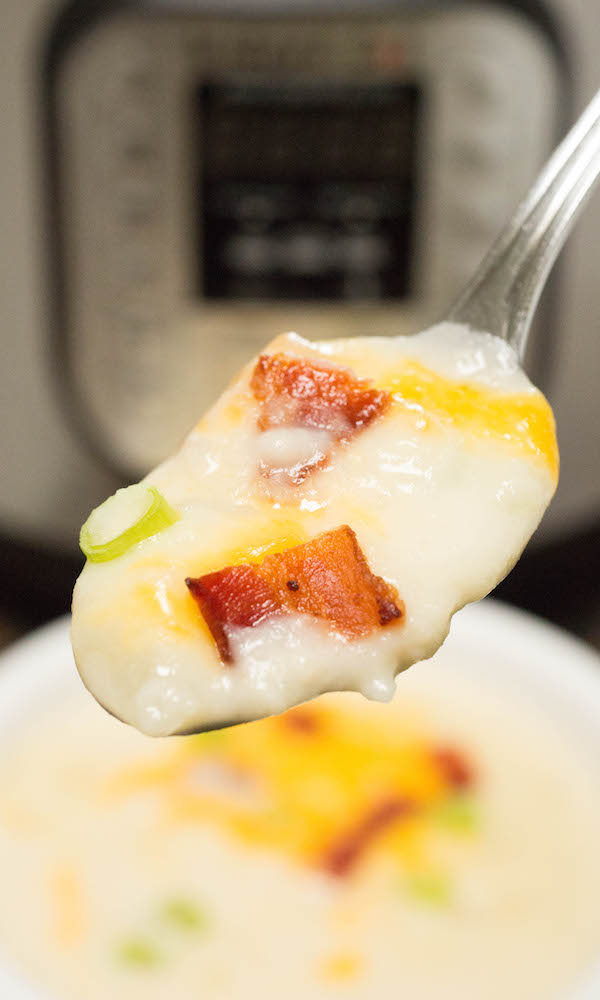 A spoonful of Instant Pot Baked Potato Soup topped with bacon, green onions, and cheese. The soup bowl and Instant Pot are out of focus in the background.