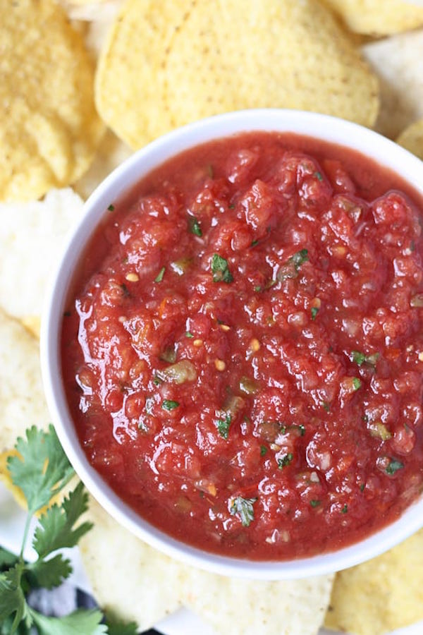 Closeup of Chilis copycat salsa in a white bowl with tortilla chips in the background