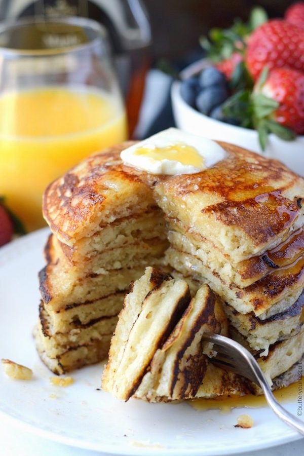 Seven cooked copycat IHOP pancakes stacked on top of each other on a white plate with butter on top.