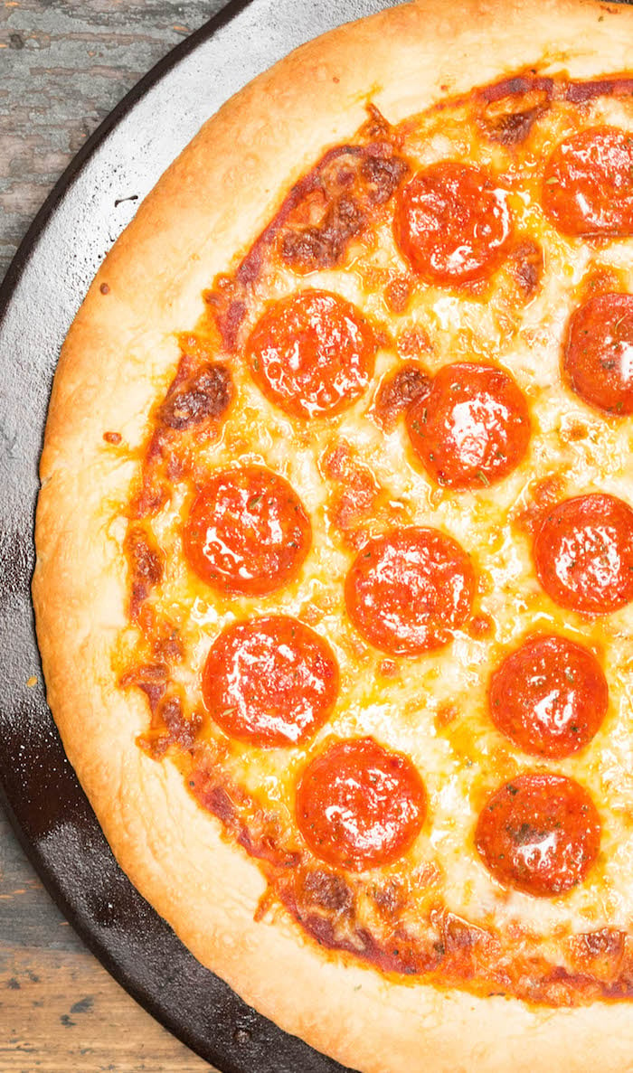 Overhead shot of a pepperoni NYC style pizza on a pizza stone.