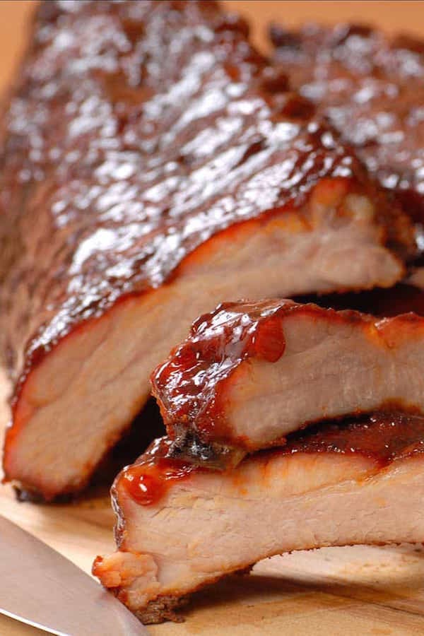 Close up of a slab of BBQ ribs with two ribs cut off and in the foreground