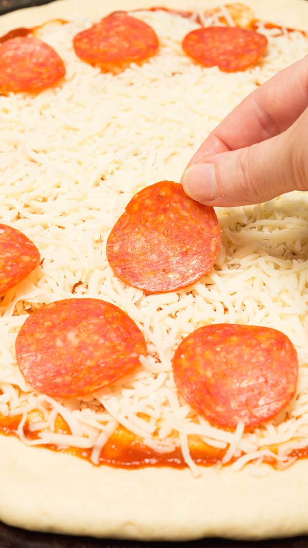 Pepperonis being places on top of mozzarella cheese on raw pizza dough.