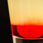 Close up of a single layered pineapple upside down cake shot on a black background. Bottom layer red, top layer yellow.