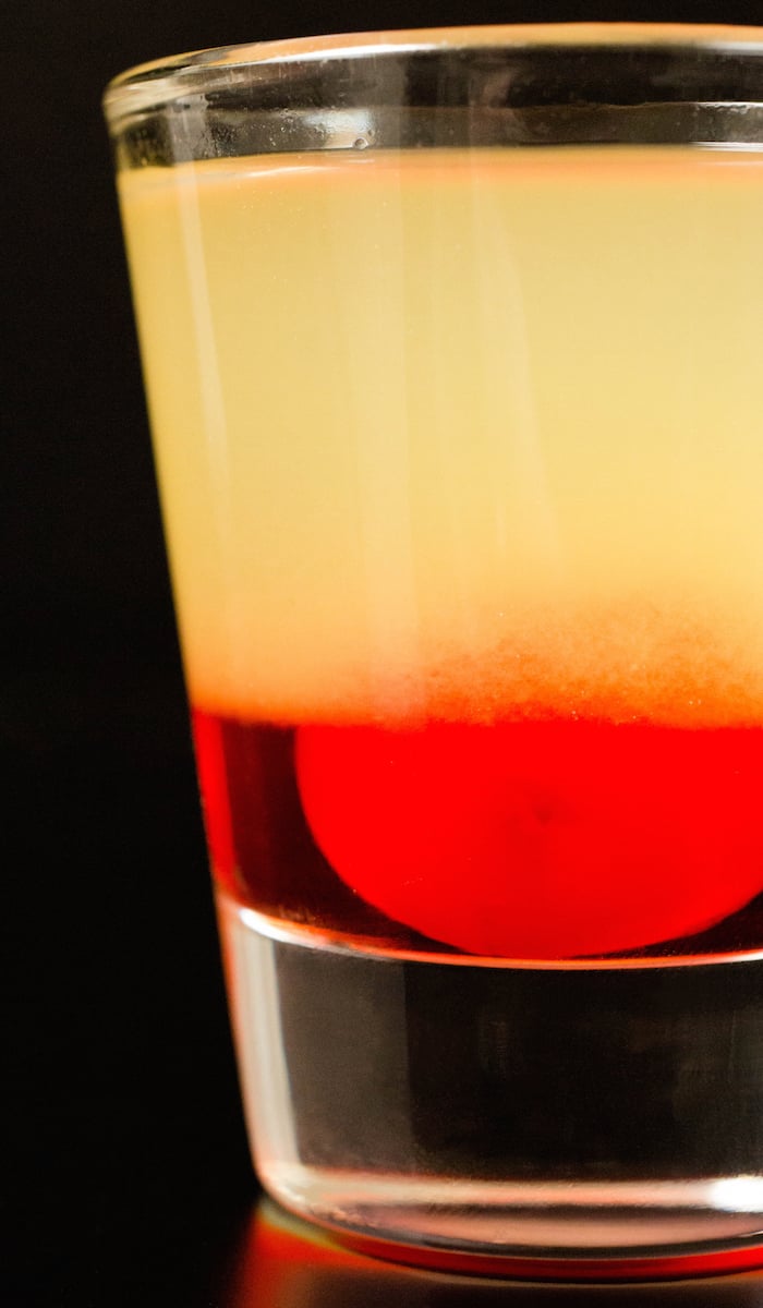 Close up of a single layered pineapple upside down cake shot on a black background. Bottom layer red, top layer yellow.