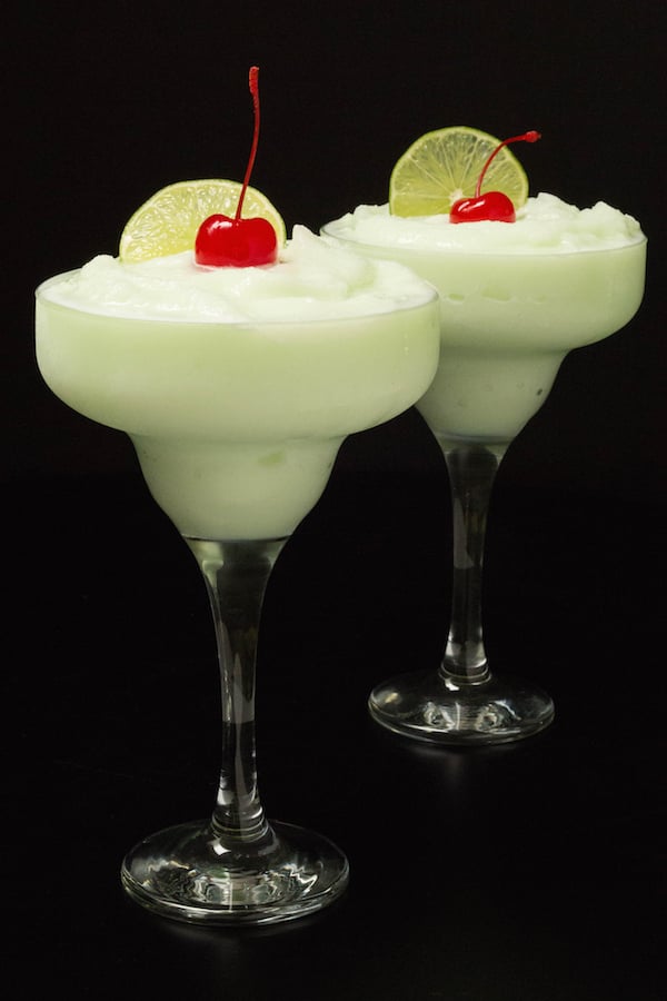 Two lime sherbet margaritas in tall margaritas glasses on a black background.