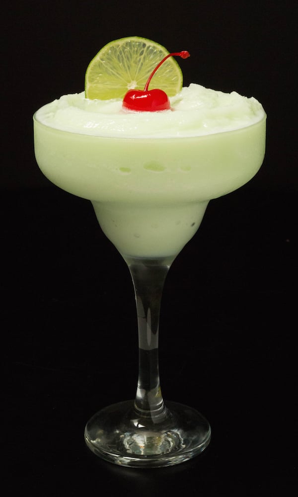 A lime sherbet margarita in a tall glass sits on a black background.