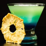 A layered blue to green Quarantiki cocktail in a glass on a blackbackground.
