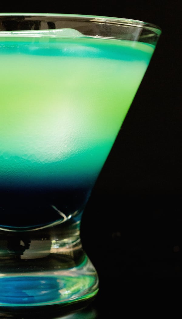 Close up of a blue and green layered qurantiki cocktail in a stemless martini glass.