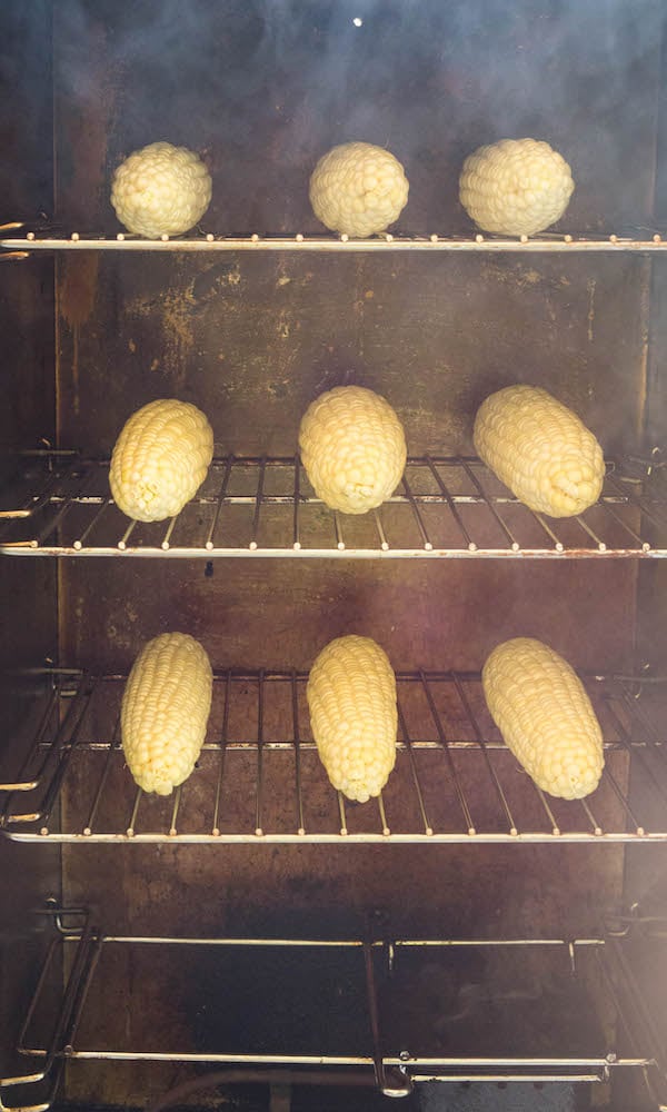 Head-on view of three racks of corn on the cob being cooked in a smoker