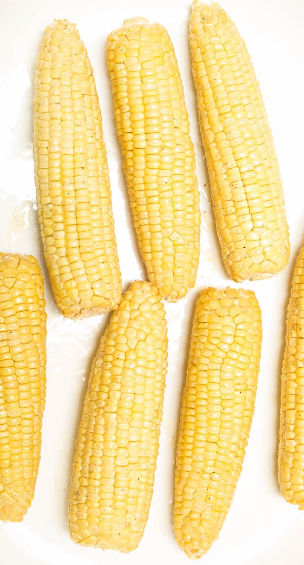 Overhead shot of seven smoked corn on the cobs on a white background