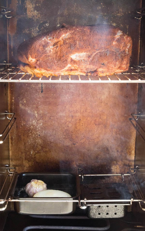 Cherry coke pork shoulder in the middle rack of a meat smoker with smoke around it. 