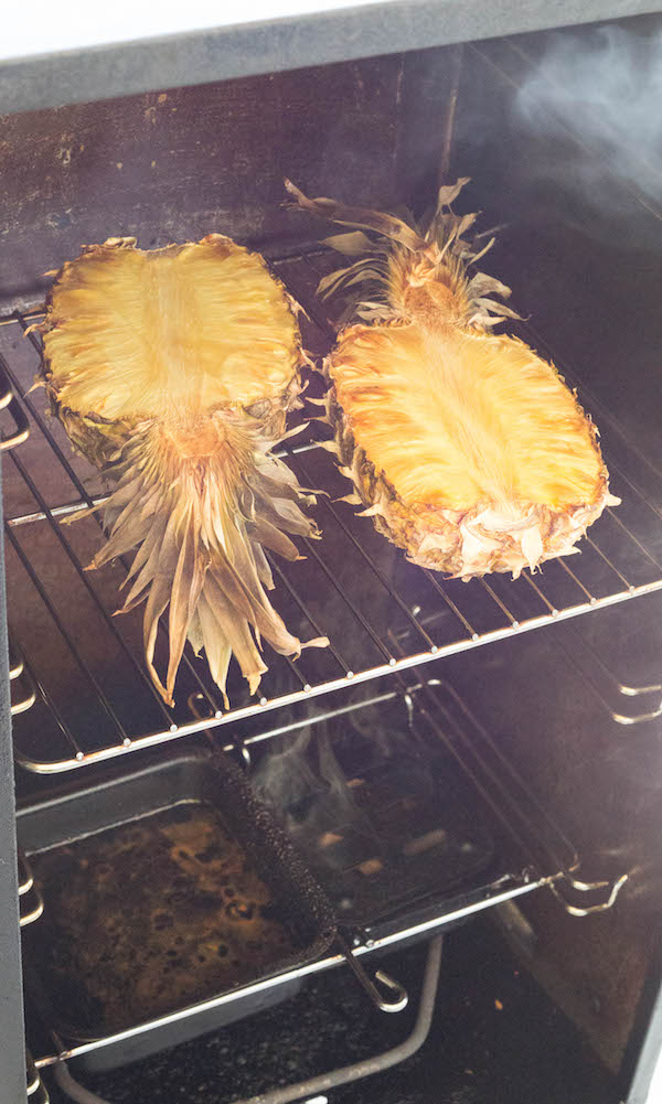A pineapple sliced in half being cooked inside a meat smoker