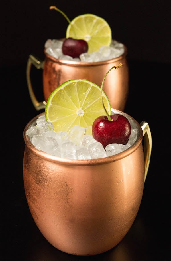 Two cherry limeade moscow mules in copper mugs on a black background