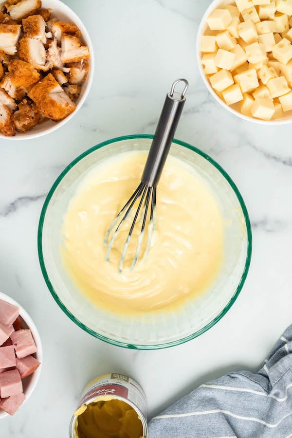 Overhead shot of popcorn chicken, swiss cheese, diced ham, and cream of chicken soup all in separate bowls on a marble board