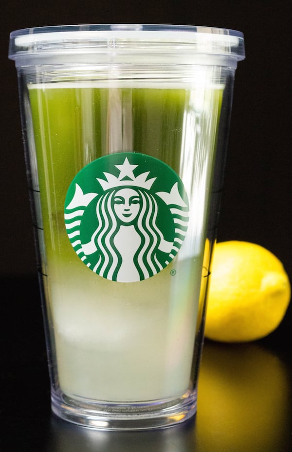 A grande starbucks cup filled with matcha lemonade. A lemon sits in the background.