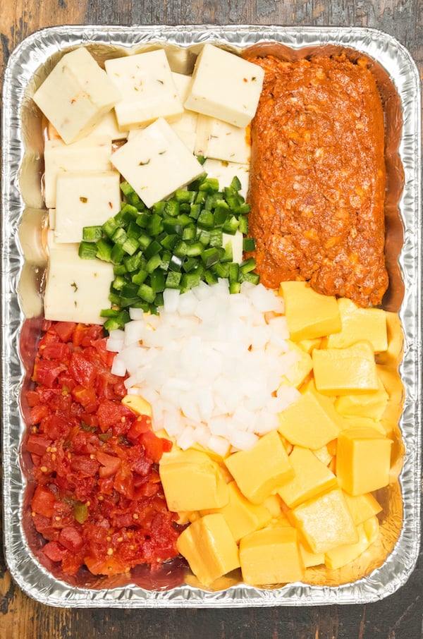 Overhead shot of a pan filled with sliced velveeta, pepper jack, jalapenos, onion, rotel, and chorizo