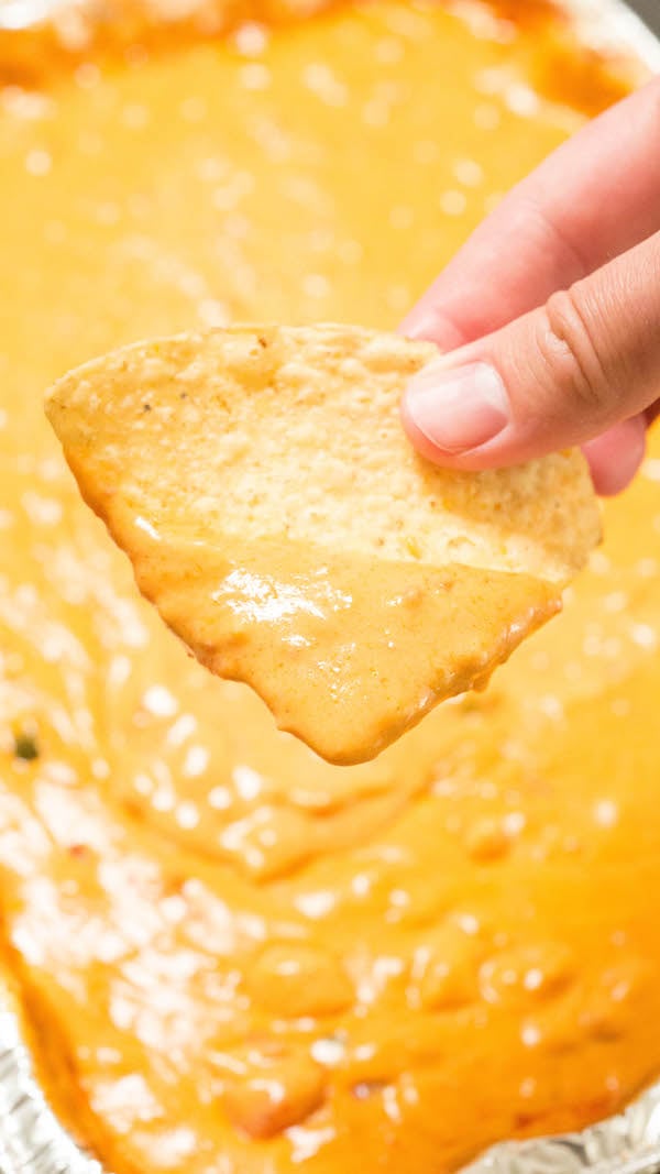 Close up of a finger holding a tortilla chip that has been dipped in smoked queso