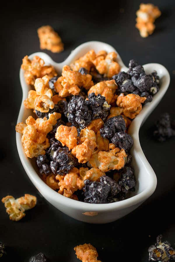 A white ghost shaped bowl filled with black and orange Halloween popcorn.