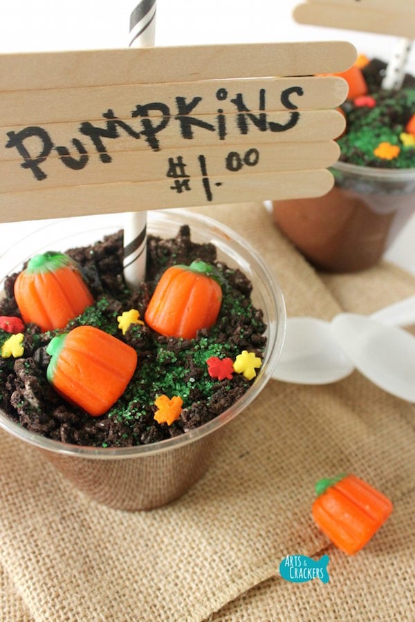 A plastic punch cup filled with pudding and crushed oreos then topped with candy to look like a pumpkin patch