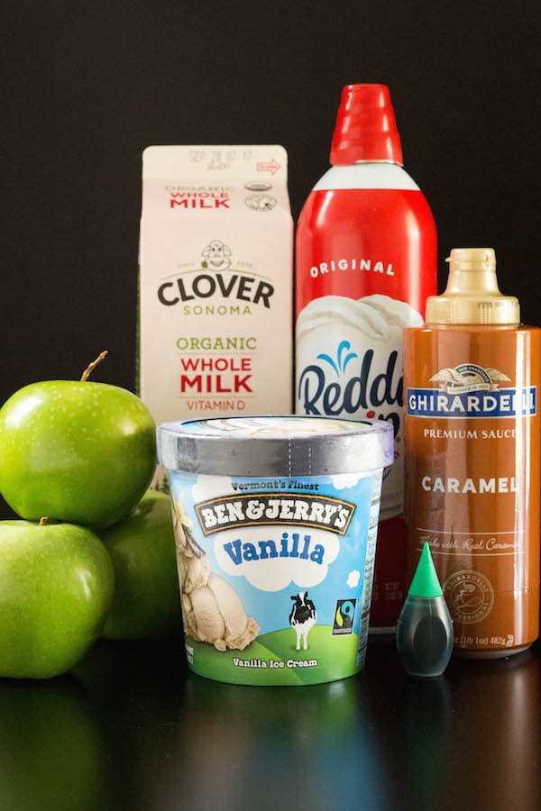 A carton of whole milk, 3 green apples, ice cream, whipped cream, and caramel on a black background