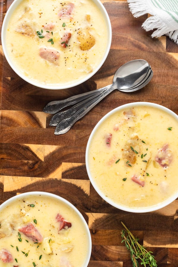 Overhead shot of three bowls of ham and potato soup on a wood cutting board