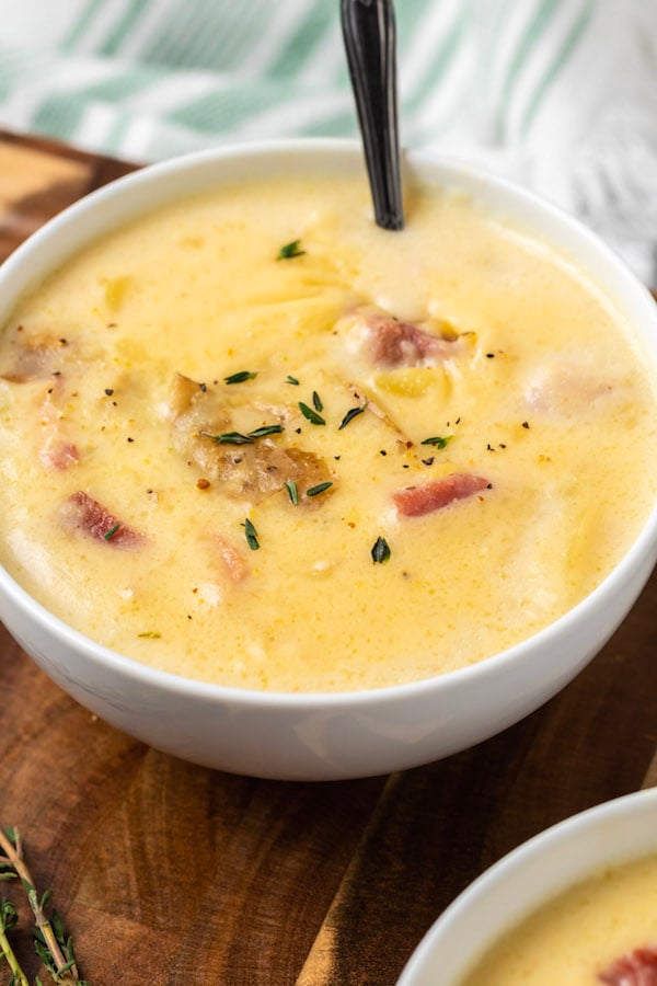 A white bowl of ham and potato soup with thyme on top and a spoon. 