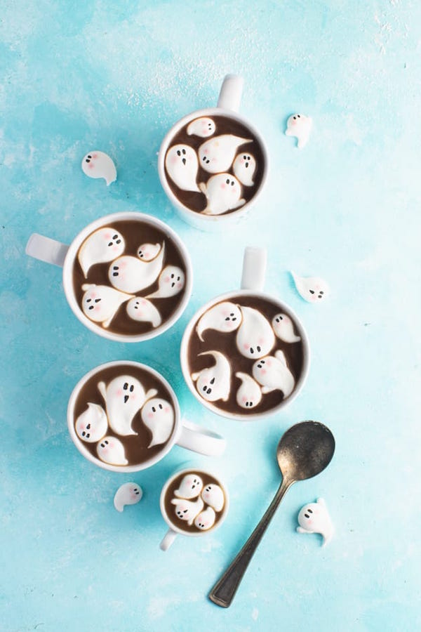 Ghost shaped marshmallows with drawn on faces on top of hot cocoa. 