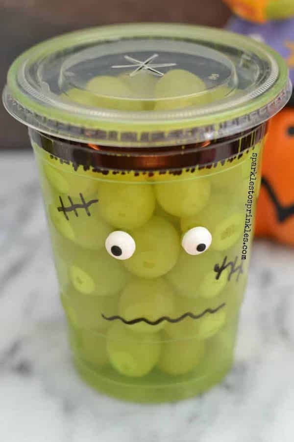 A plastic cup colored with a sharpie then filled with green grapes. Looks like a frankenstein monster. 