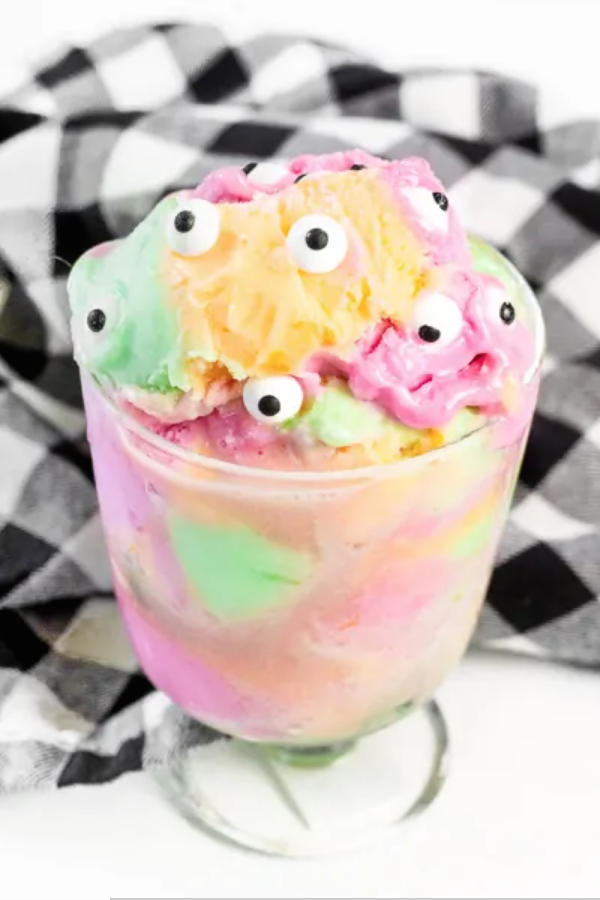 Mulitcolored sherbet ice cream in a glass cup with monster eyeballs on top. 