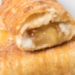 Close up of an apple cheesecake chimichanga that has been cut open on the end to show the cream cheese and apple pie filling
