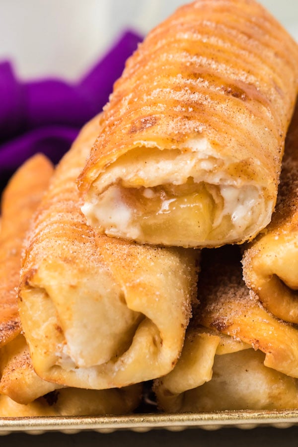 Six Cheesecake Chimichangas are stacked in a pyramid on white plate. 