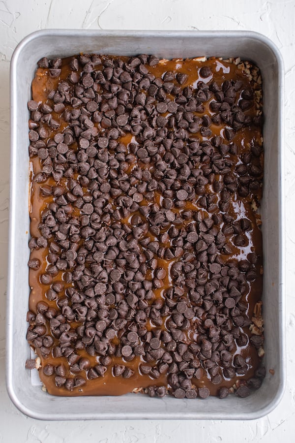 Overhead view of a 9x13 pan filled with butter toffee ingredients, a layer of chocolate chips on top