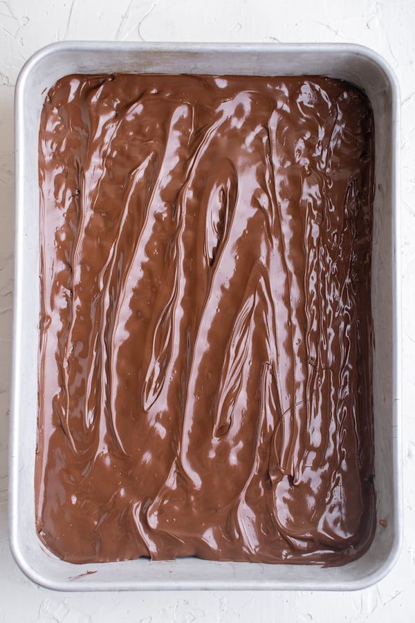 Overhead view of a 9x13 pan with a layer of warm chocolate chips that have been smoothed over with a silicone spatula