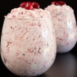 Two stemless wine glasses filled with cranberry fluff dessert on a black background