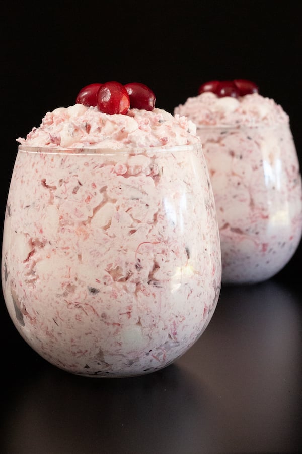 Two stemless wine glasses filled with cranberry fluff dessert on a black background