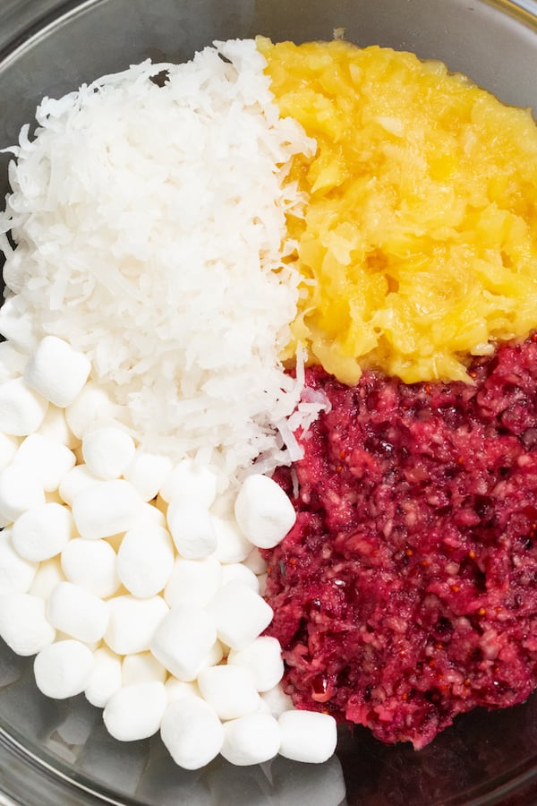 Overhead shot of cranberry fluff ingredients in a mixing bowl - mini marshmallows, shredded coconut, processed cranberries, and shredded pineapple