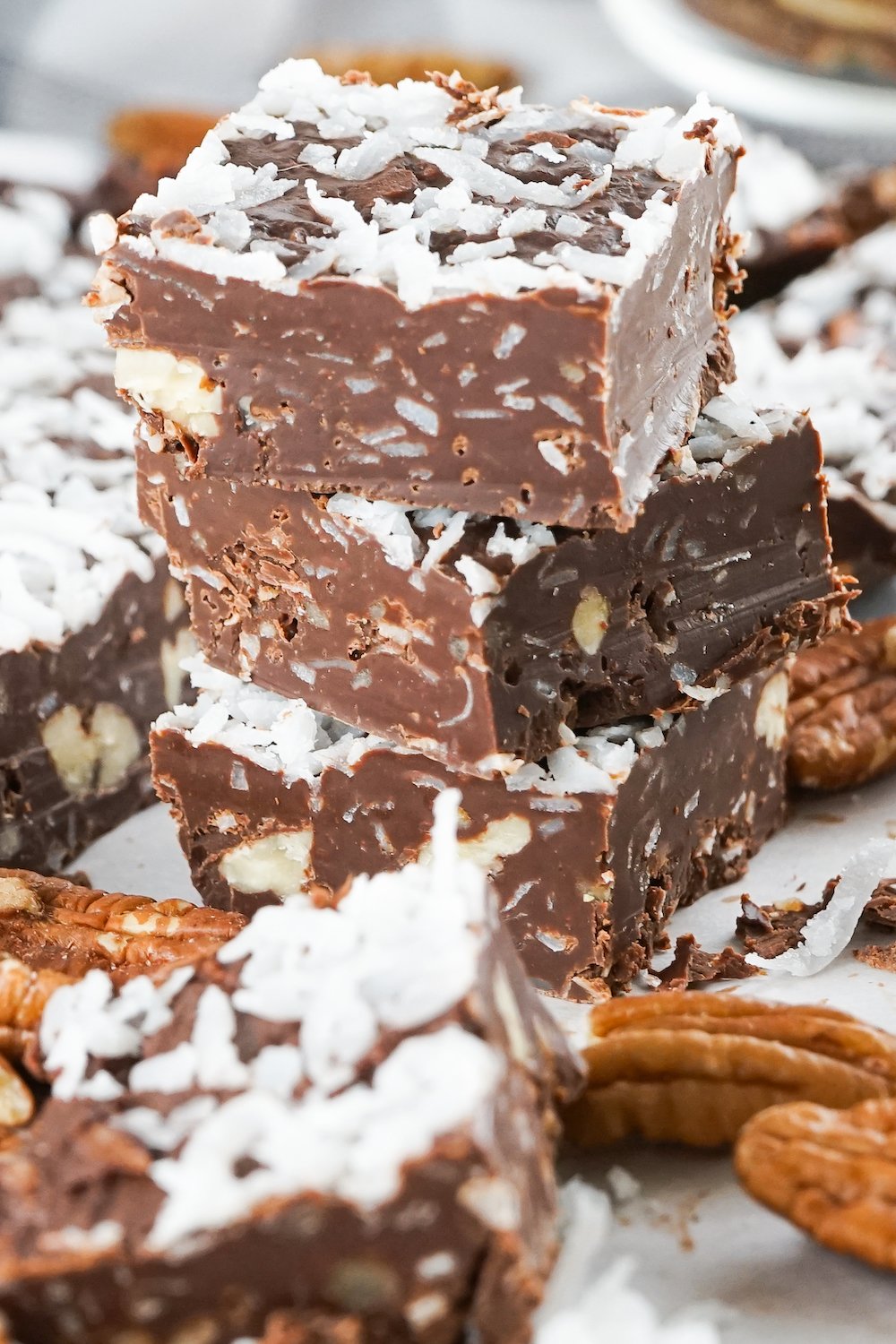 A stack of three pieces of german chocolate fudge on a white background with pecans as decoration
