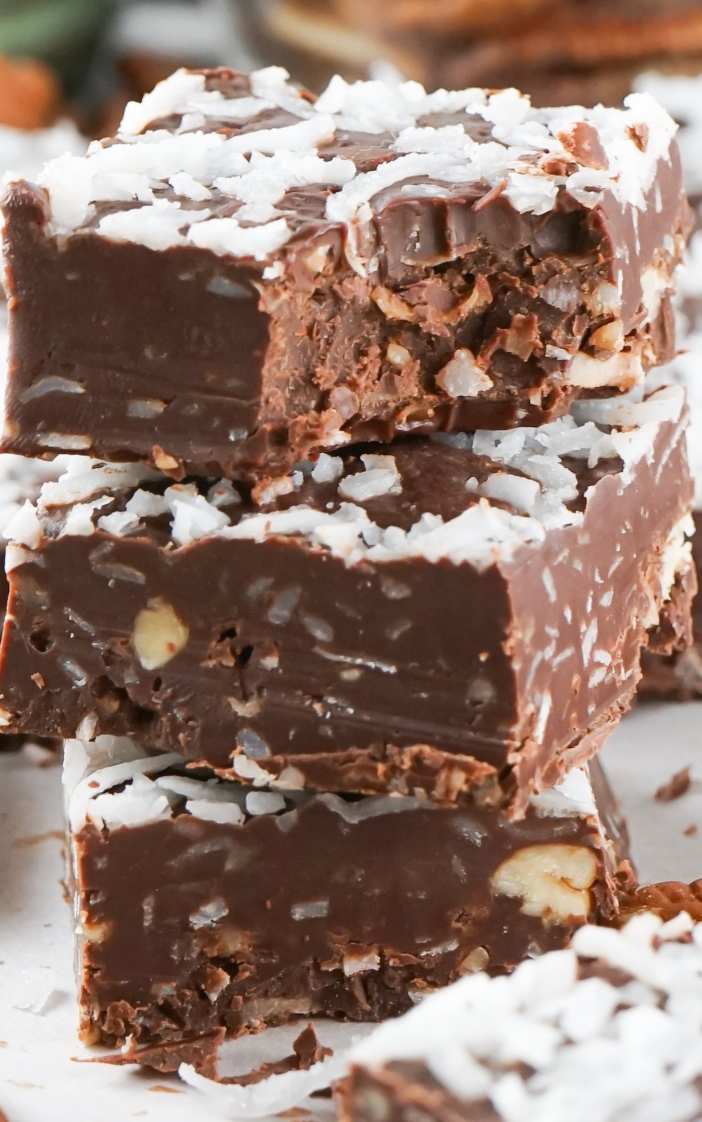 Three pieces of german chocolate cake fudge stacked on top of each other. The top piece has a bite taken out of it.