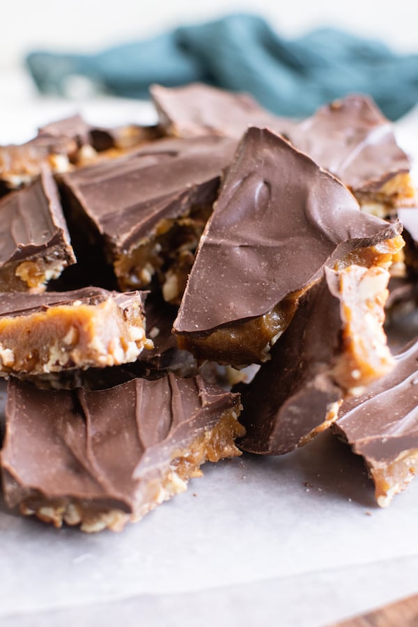 Cut pieces of homemade butter toffee are displayed stacked on top of one another on to of parchment paper