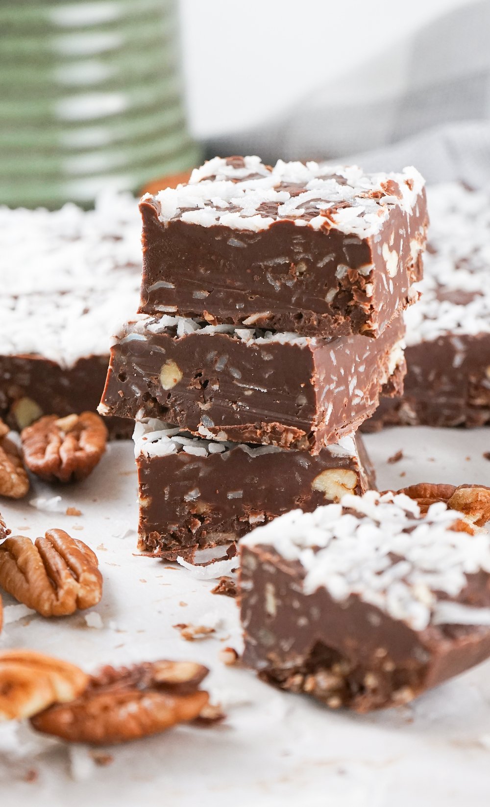 Three stacked pieces of german chocolate fudge surrounded by single pieces of fudge and pecans on a white background