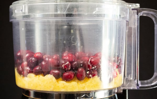 Fresh cranberries and crushed pineapple sit in a food processor on a black background