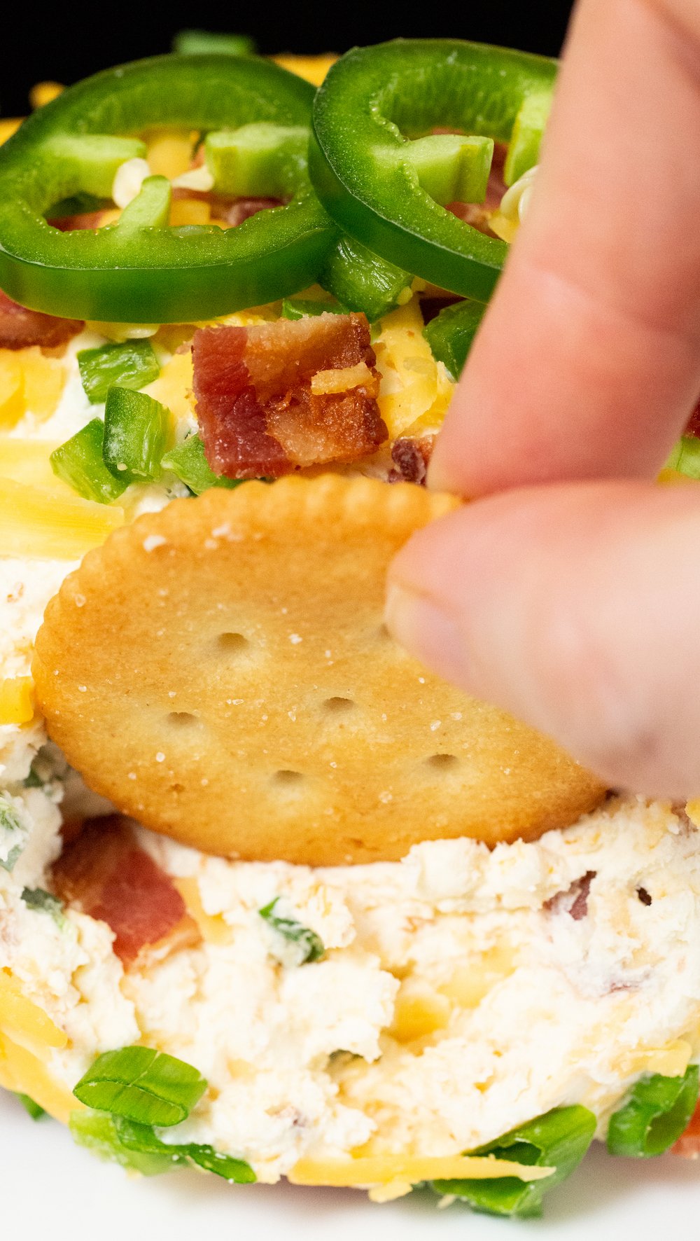 Close up of a ritz cracker being dipped in a jalapeno popper cheese ball