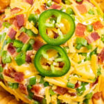 Overhead shot of a jalapeno popper cheeseball covered in shredded cheddar, diced jalapeños, and chopped bacon