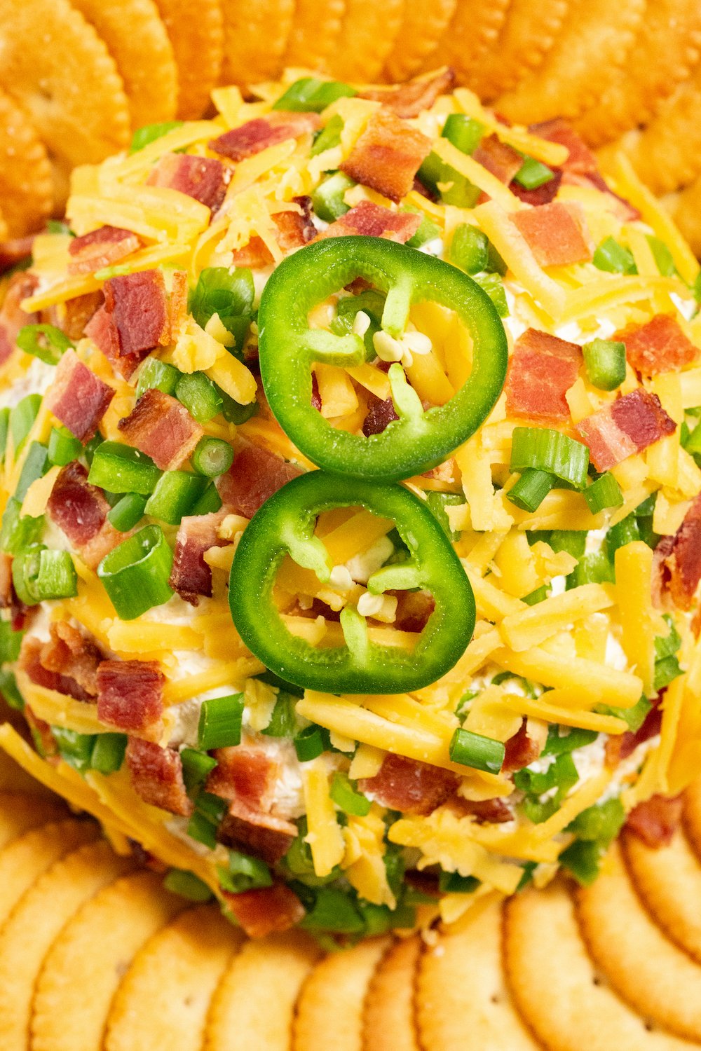 Overhead shot of a jalapeno popper cheeseball covered in shredded cheddar, diced jalapeños, and chopped bacon