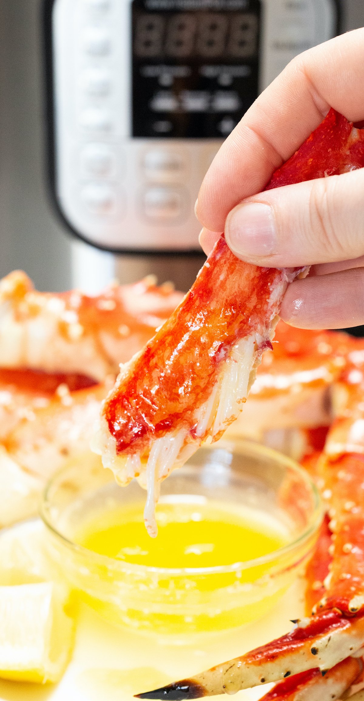 Crab leg meat is being dipped in a bowl of butter that is sitting in front of an Instant Pot