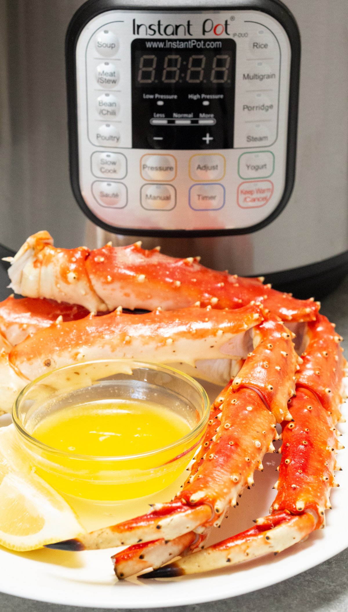 Three cooked crab legs sit on a plate with butter in front of an Instant Pot