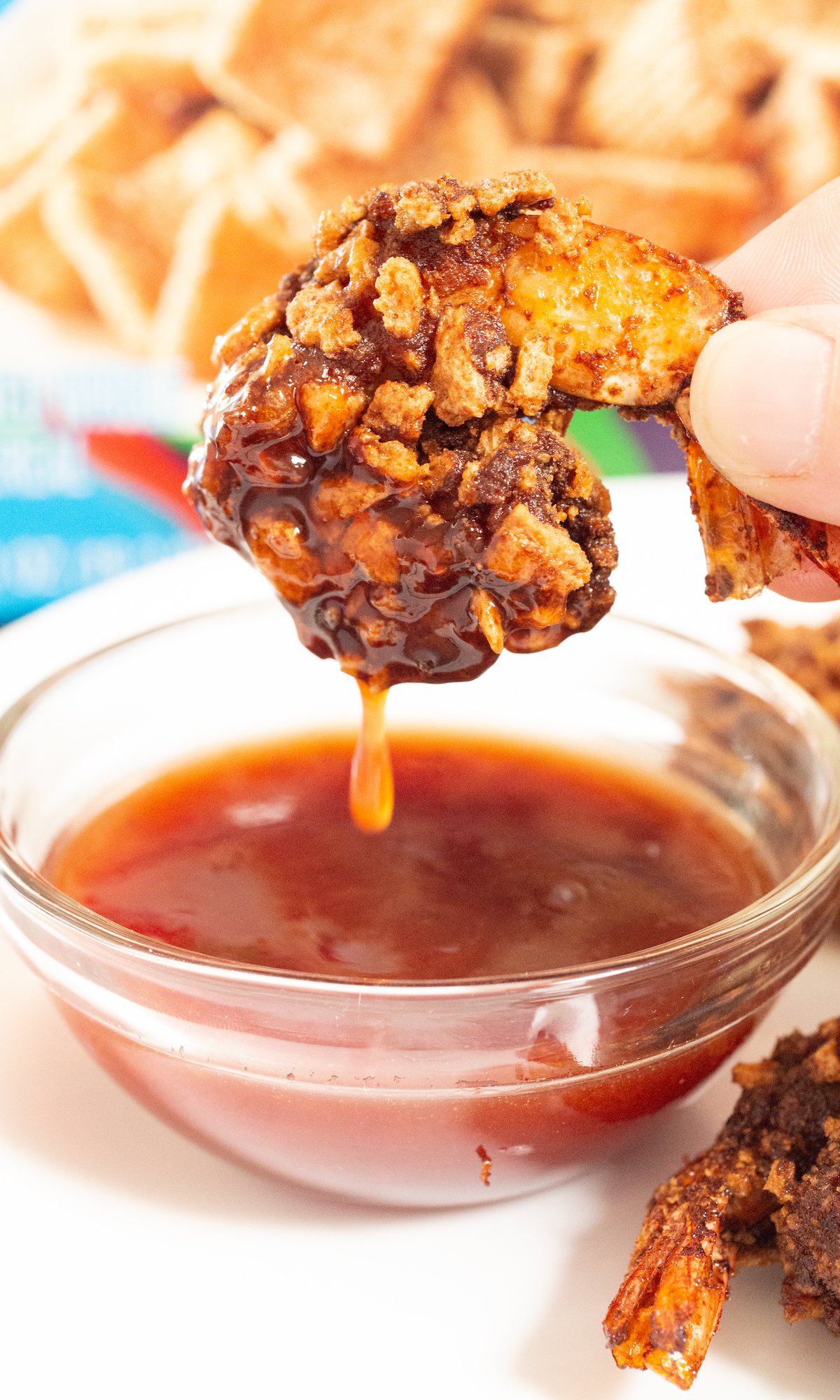 Close-up of a shrimp that's been breaded with cinnamon toast crunch then deep-fried being dipped in a strawberry habanero sauce. 