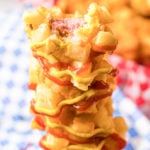 A corn dog that's covered in a french fry batter and drizzled with mustard and ketchup has a bite taken out of it.