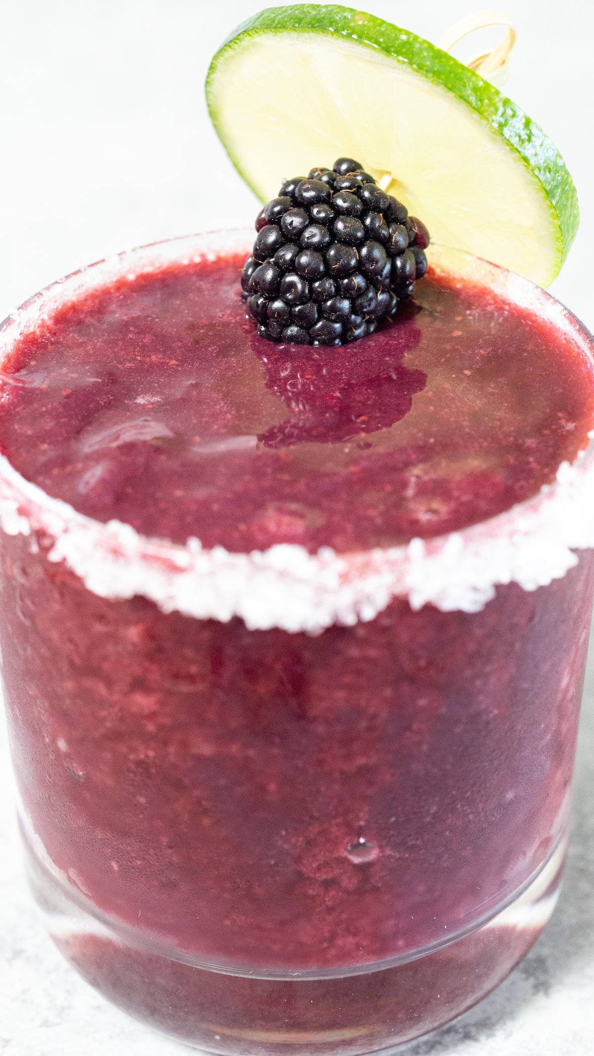 A purple blackberry margarita in a short glass garnished with a blackberry and lime wheel.